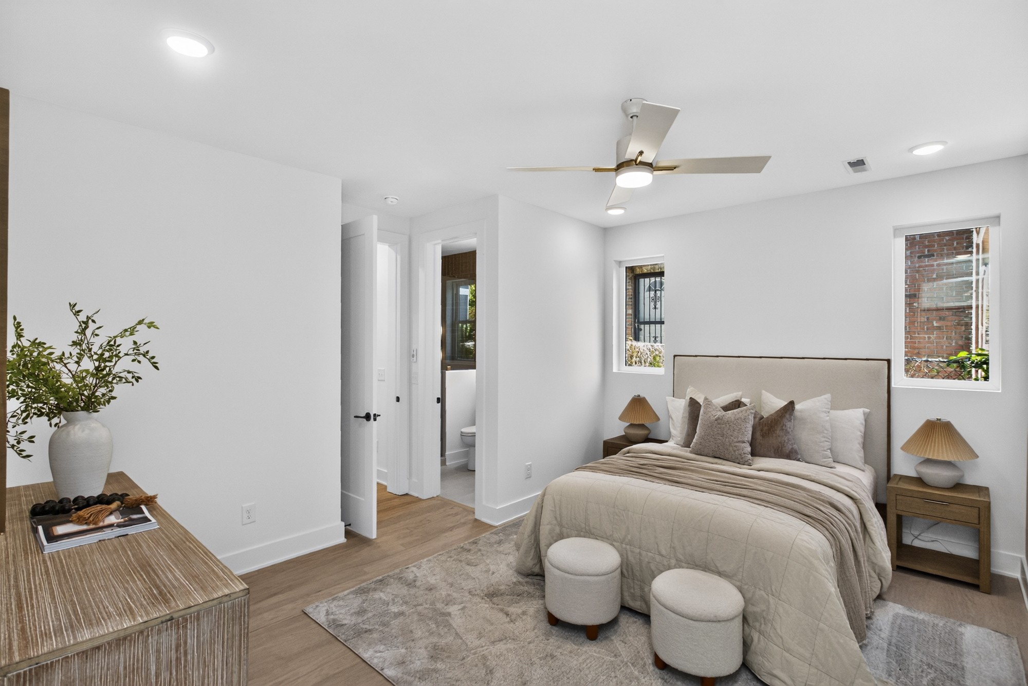 Staged bedroom with a neutral upholstered bed, matching nightstands, and two round stools.