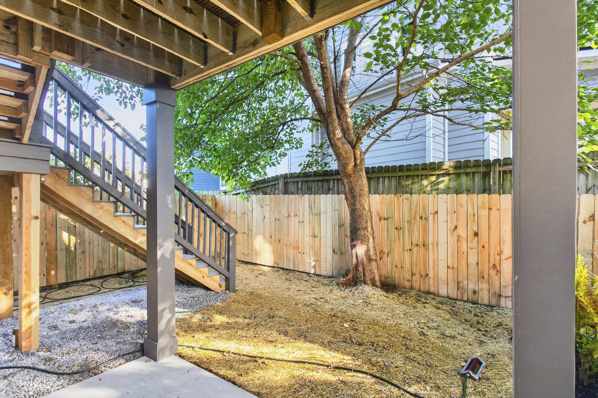 Fenced backyard with stairs from a raised deck and a large leafy tree.