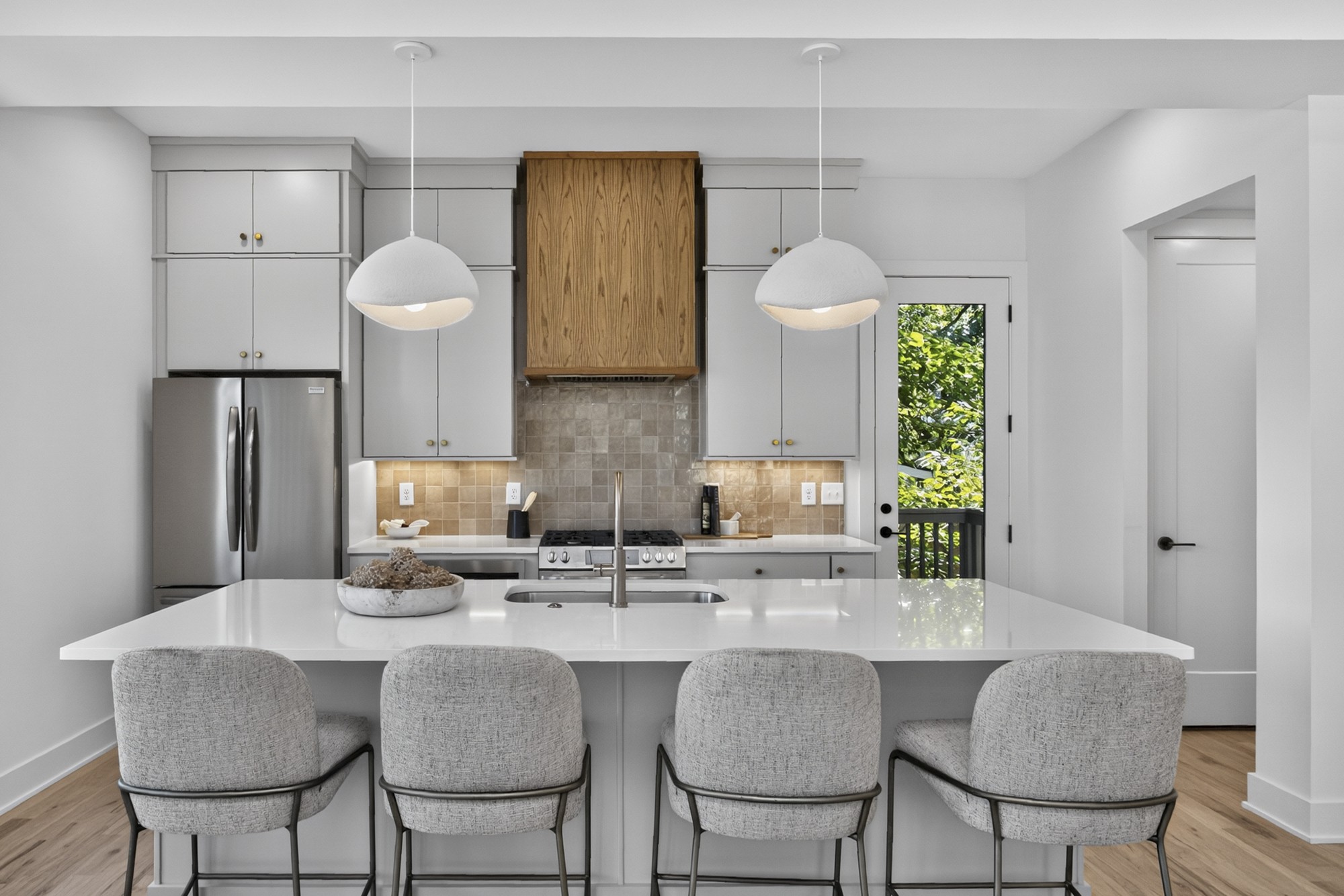 Kitchen with a large white island, four upholstered stools, and a wood range hood.