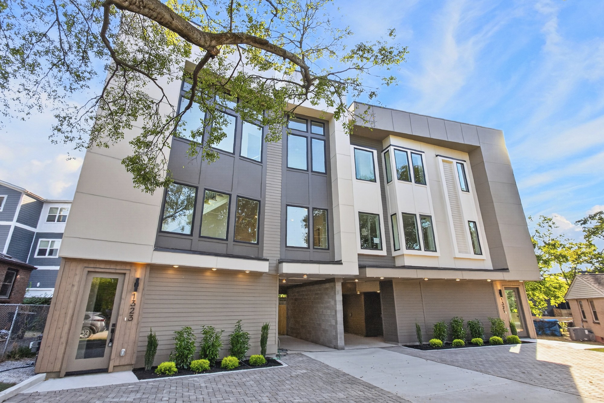 Modern multi-story residence with a gray-and-white facade, large windows, and covered parking.
