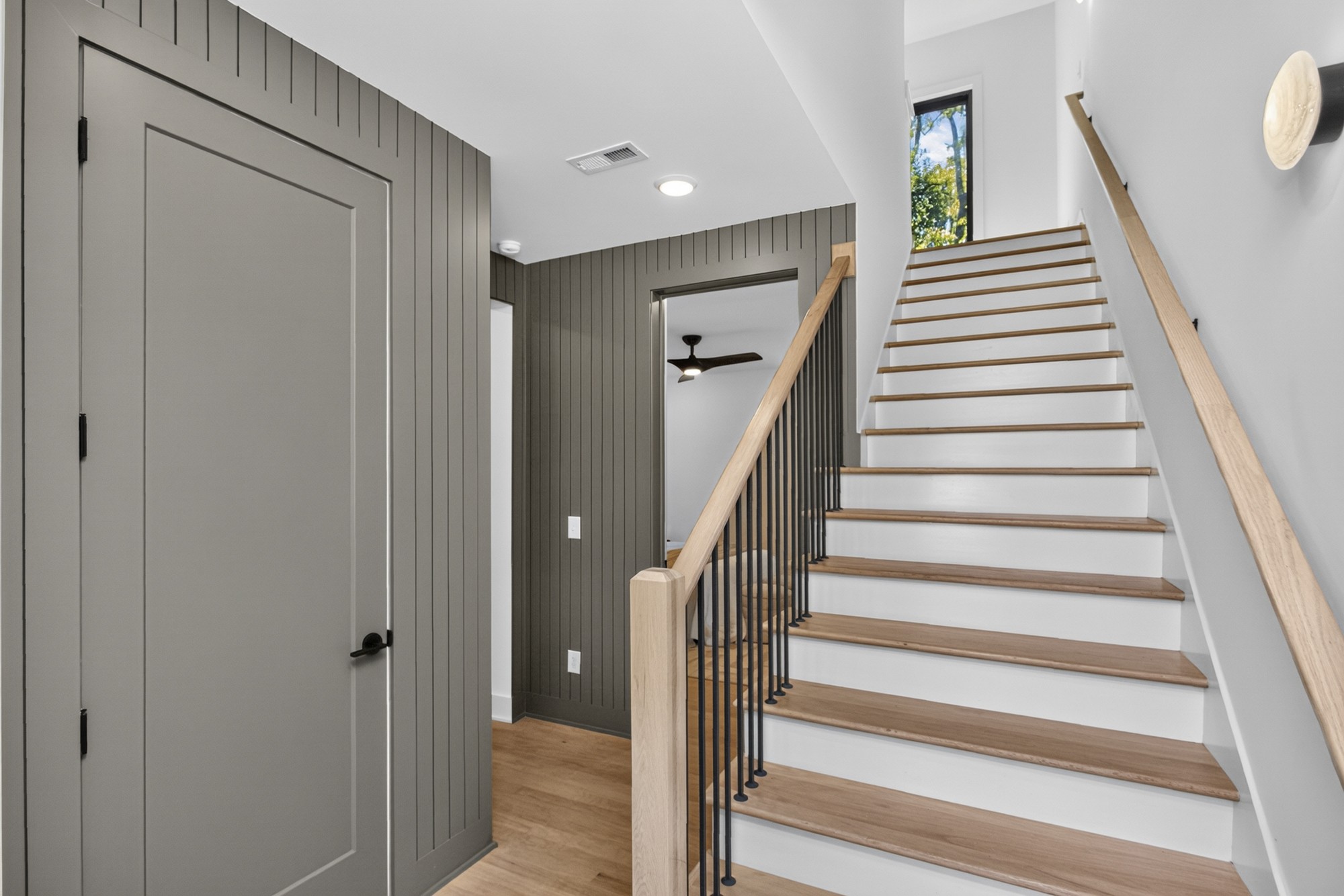 Staircase with white risers, oak treads, black balusters, and a tall window at the landing.