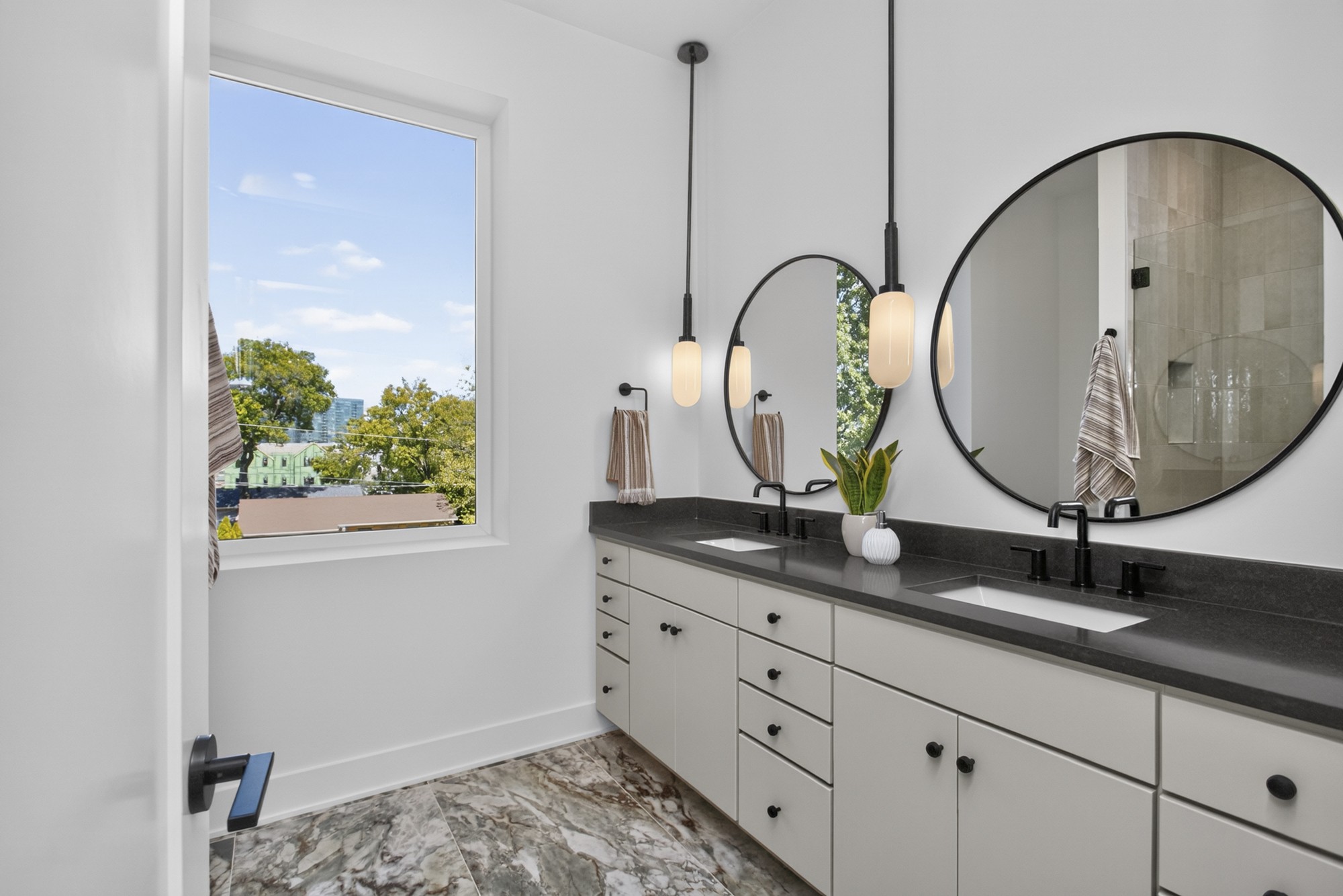 Bathroom with a double-sink vanity, round mirrors, pendant lights, and a large window.