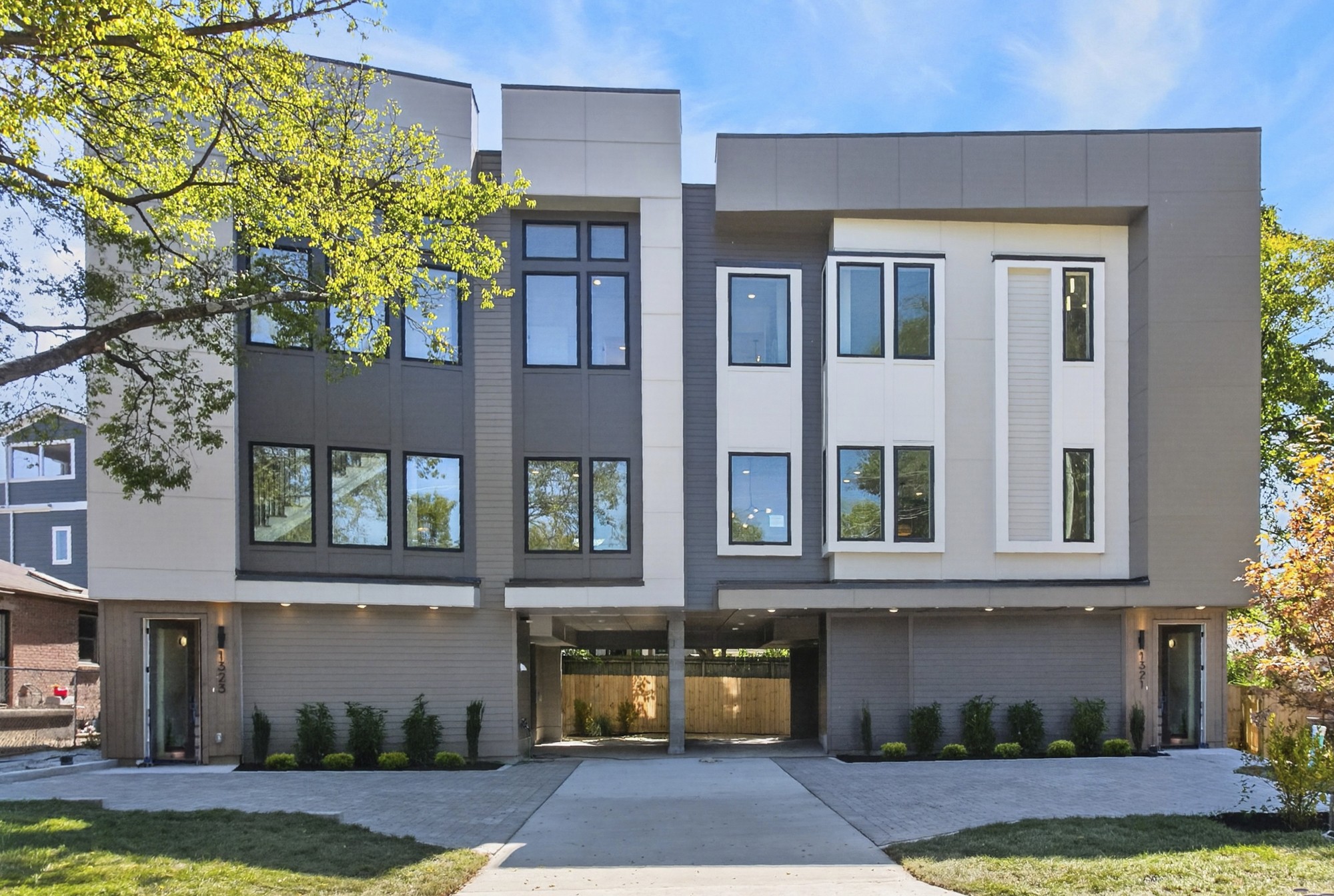 Modern multi-story home with gray and white siding, tall windows, and a covered driveway.