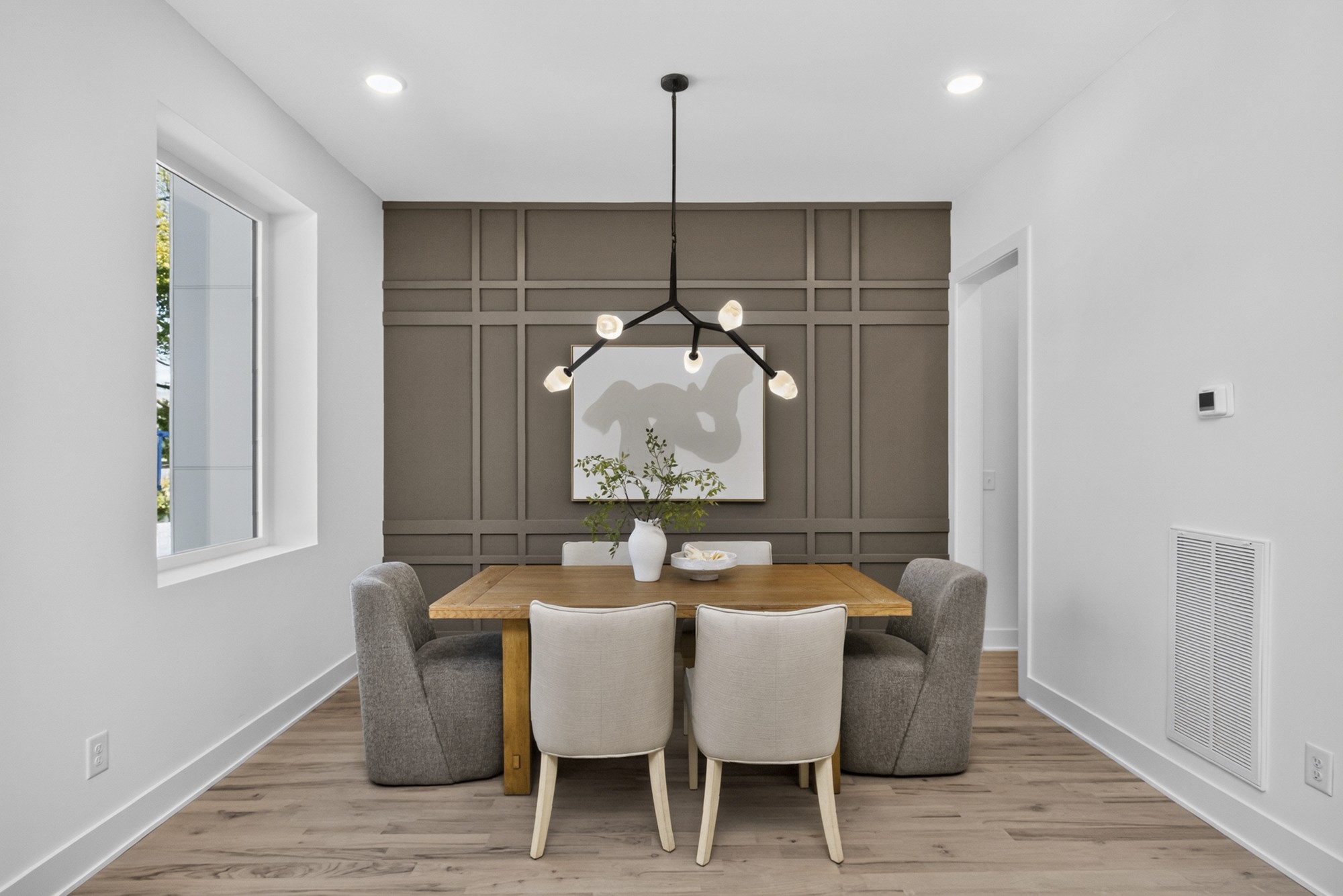 Dining room with a paneled taupe accent wall, wood table, upholstered chairs, and sculptural pendant light.