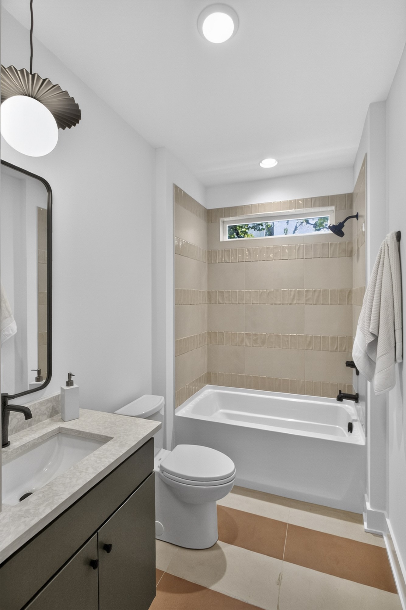 Bathroom with tiled tub surround, narrow window, vanity, and toilet.