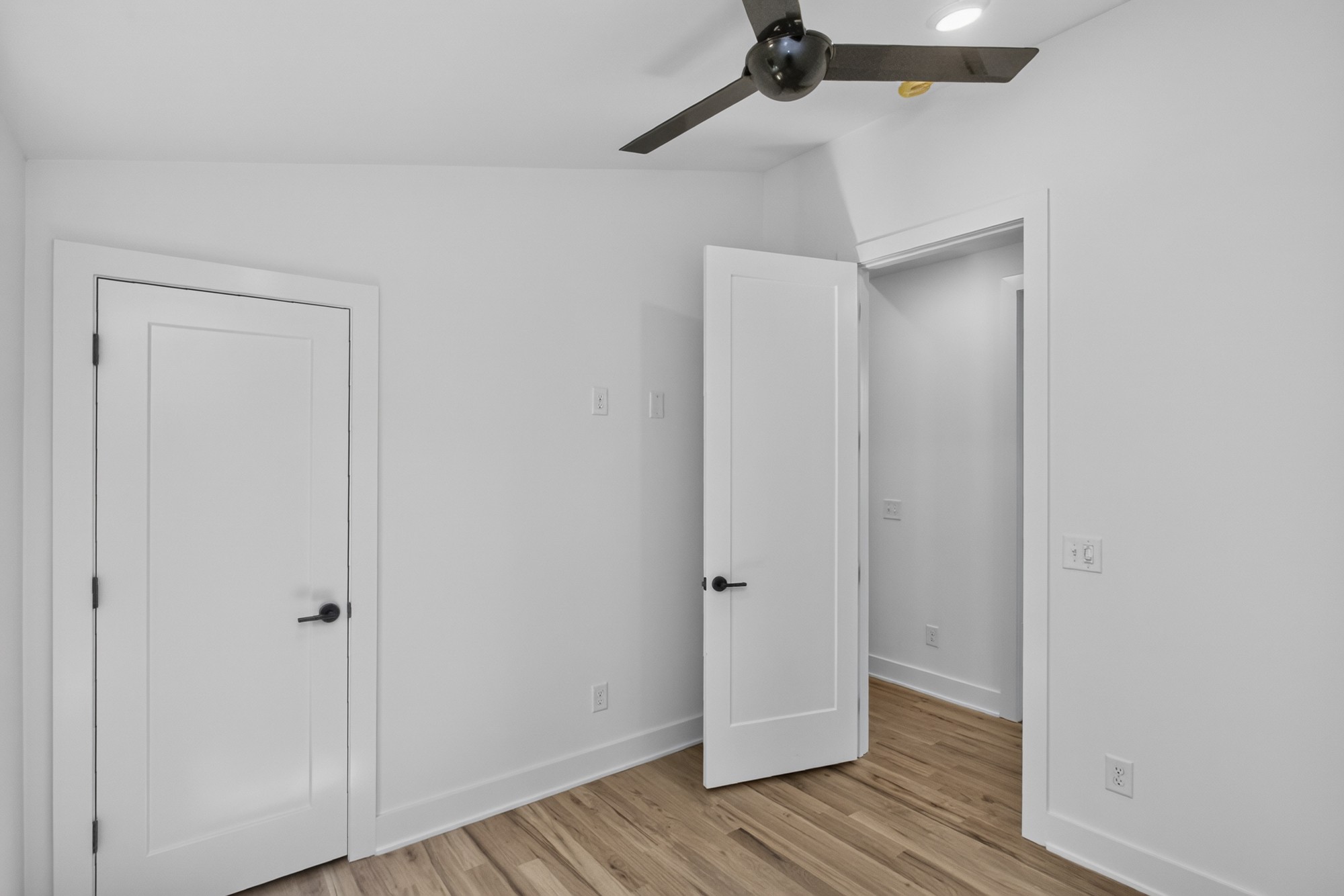 Empty room with wood flooring, white paneled doors, and a ceiling fan.