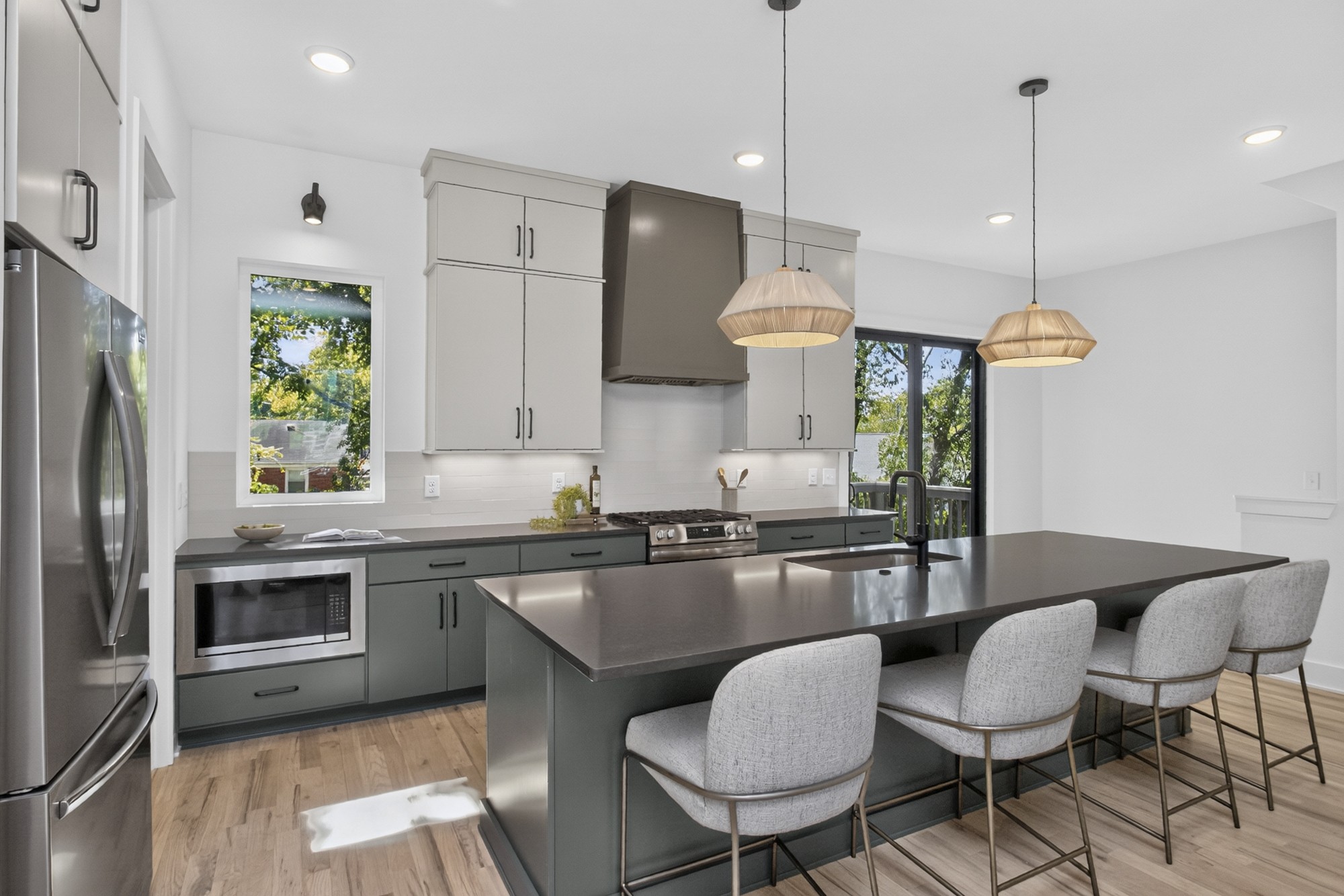 Modern kitchen with a large island, gray cabinetry, stainless appliances, and three bar stools.
