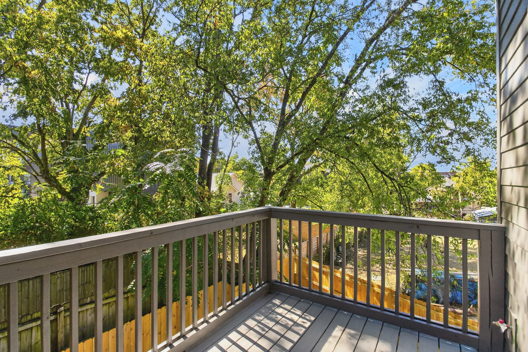 Elevated deck with gray railings overlooking leafy trees and a fenced yard.