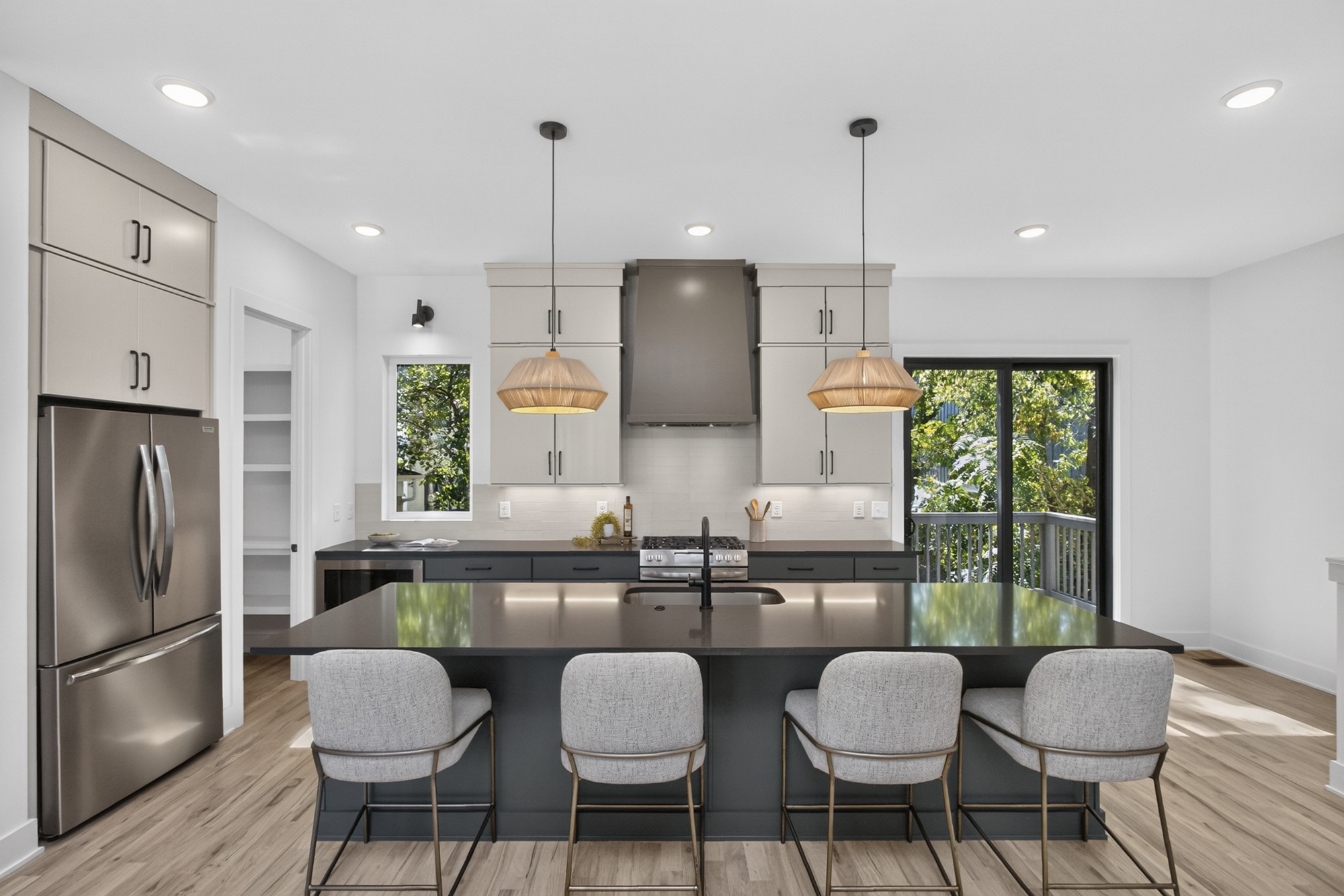 Modern kitchen with a large island, four bar stools, stainless steel appliances, and sliding doors to a deck.