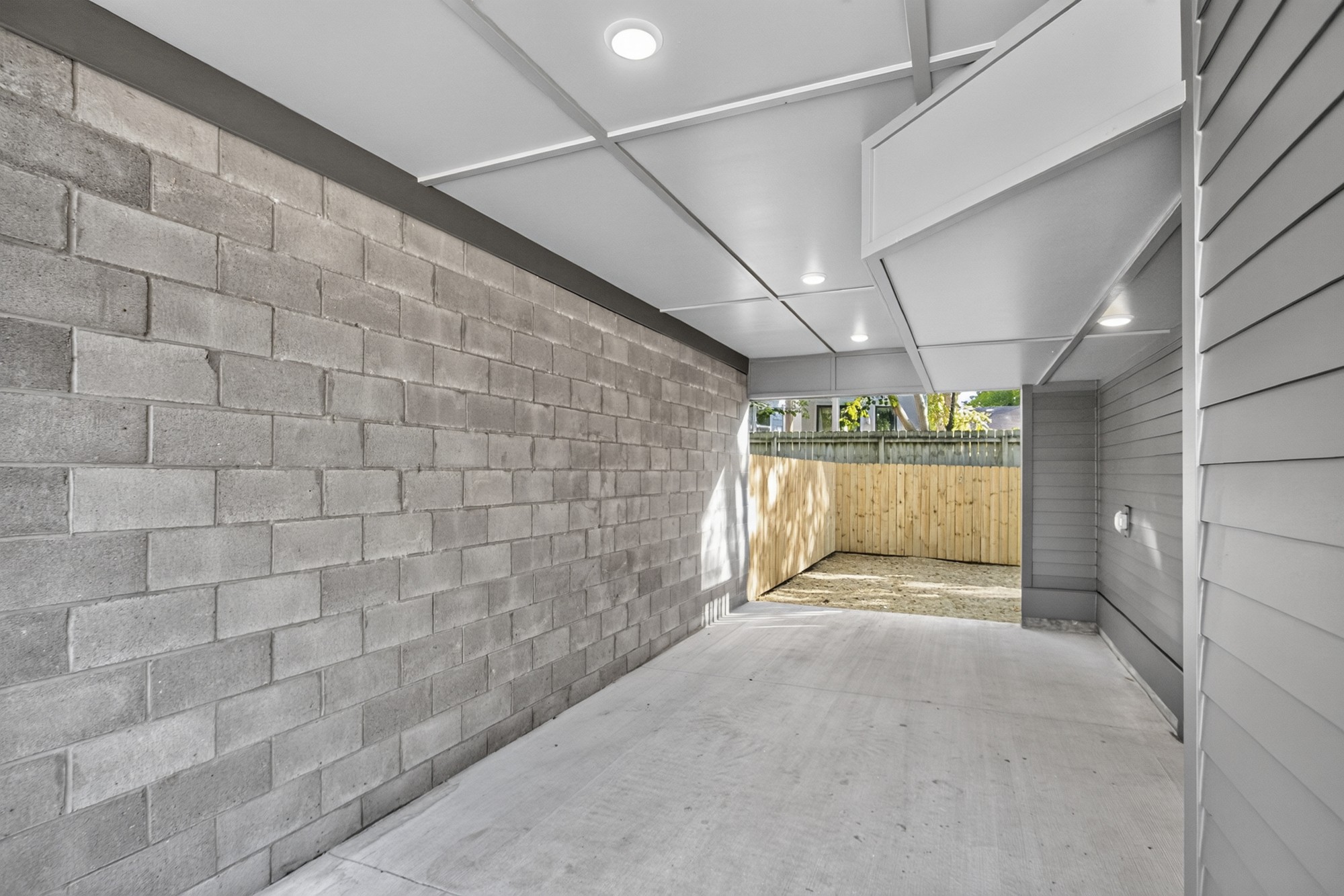 Covered concrete walkway beside a home, with block walls and a fenced yard at the far end.