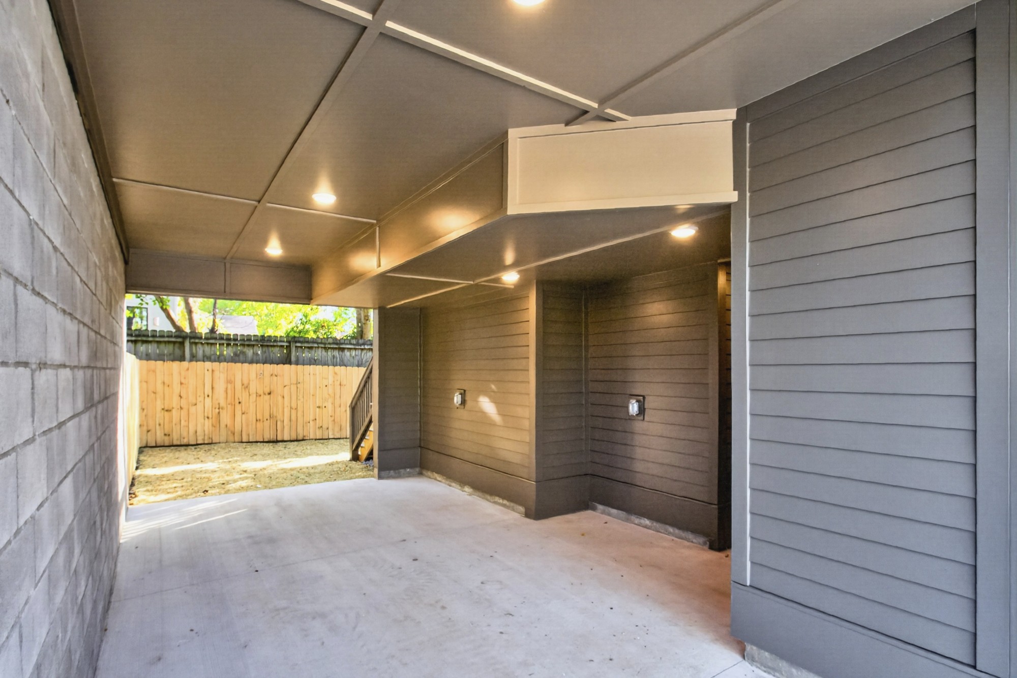 Covered carport with a concrete floor, recessed lights, and a wooden privacy fence.
