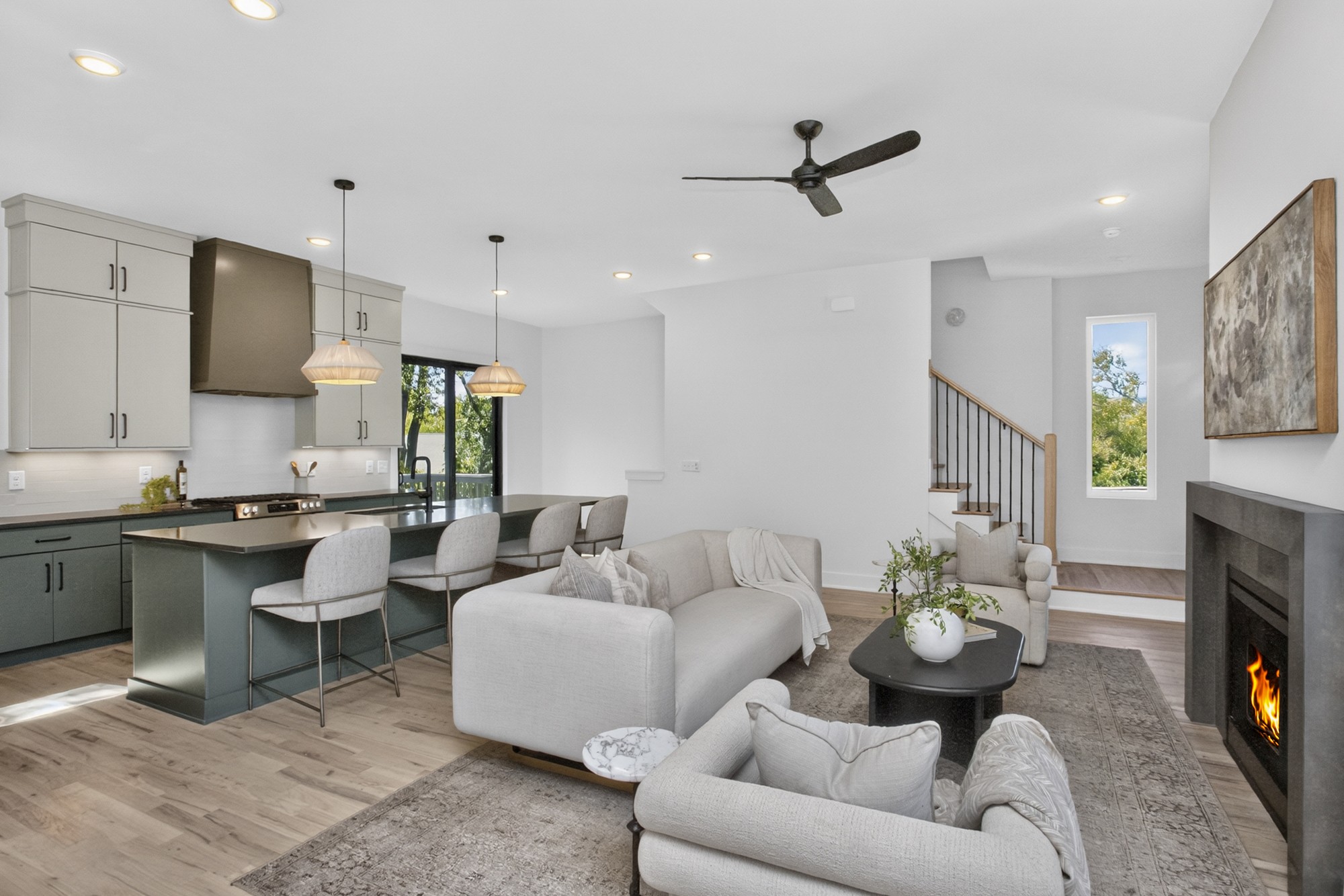 Open-plan living room and kitchen with a fireplace, dark island, and light furnishings.