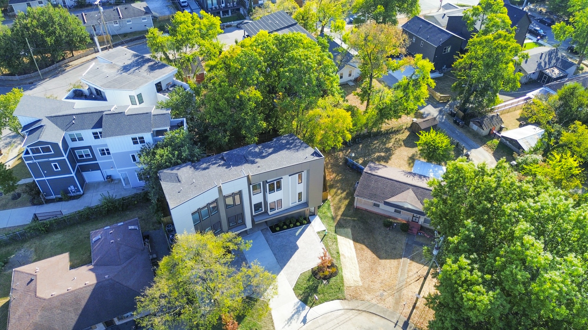 Aerial view of a modern three-story home among leafy trees and neighboring houses.