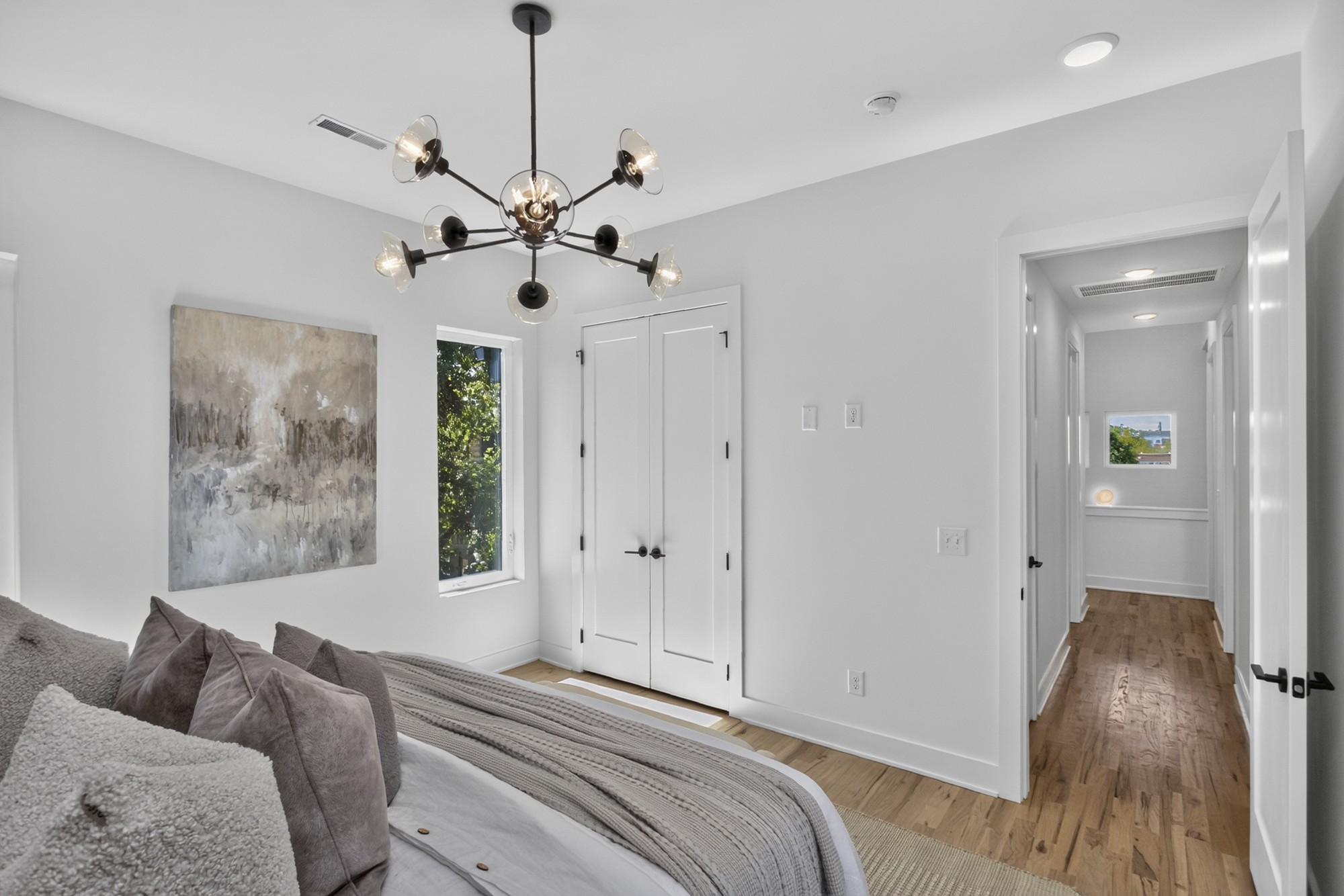 Bright bedroom with layered gray bedding, a modern chandelier, and hardwood floors.