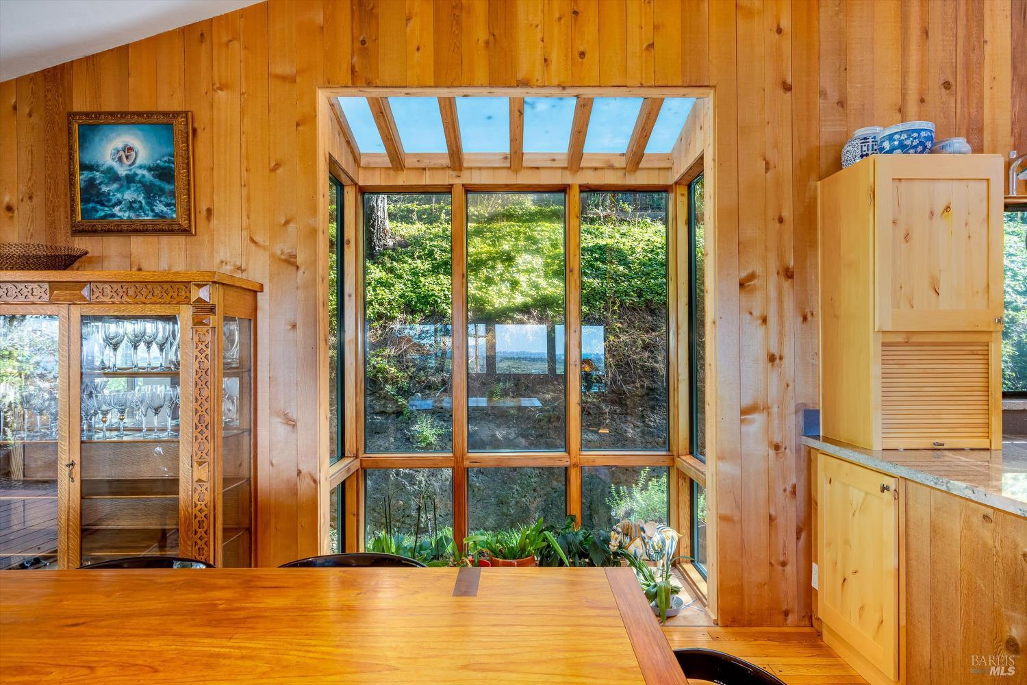Wood-paneled dining area with a skylight and tall windows overlooking greenery.