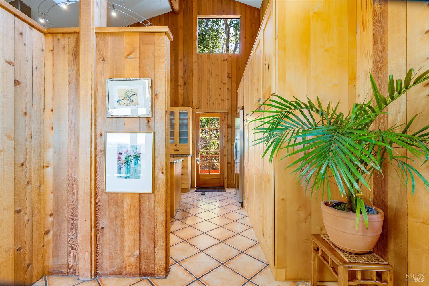 Wood-paneled hallway leading into a kitchen, with terracotta tile, built-in cabinets, and a potted palm.