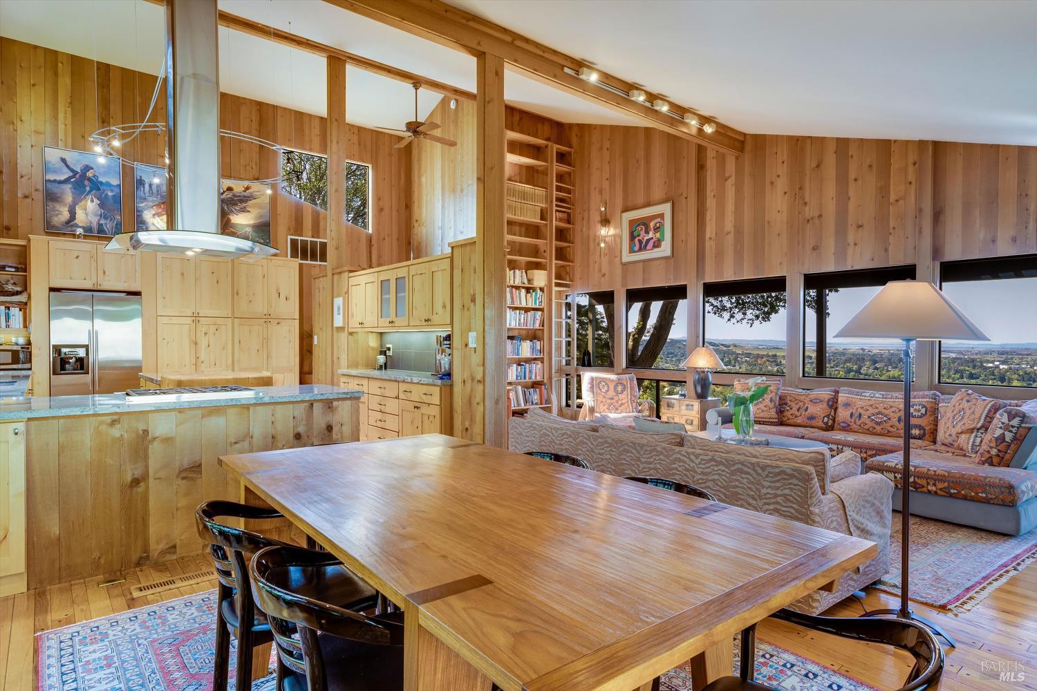 Open-plan kitchen, dining, and living area with wood-paneled walls and broad valley views through large windows.