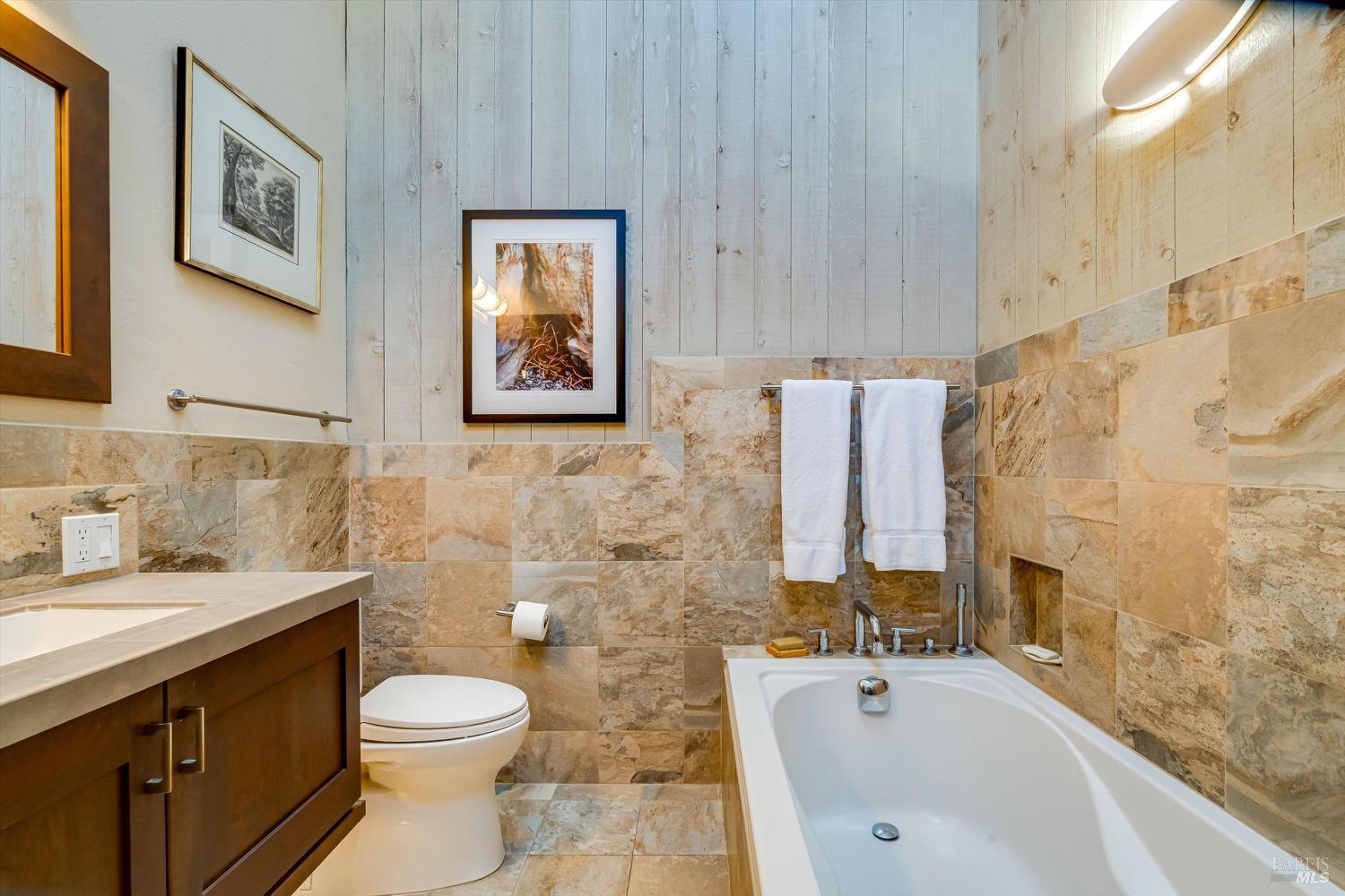 Bathroom with a white bathtub, stone tile walls, and dark wood vanity.