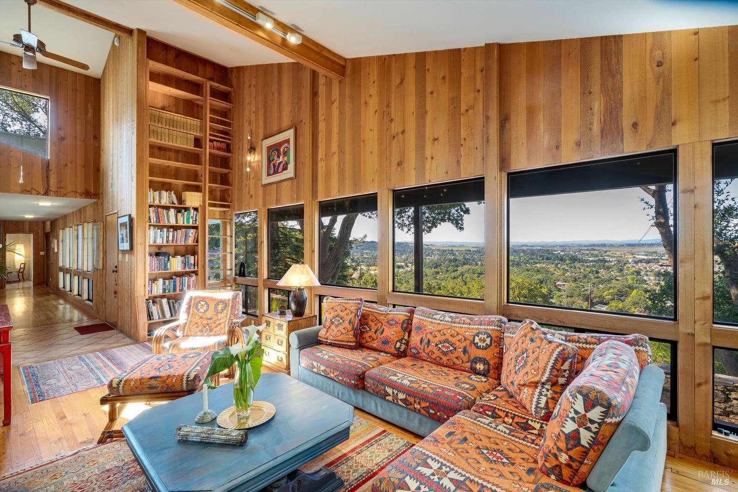 Wood-paneled living room with a built-in bookcase and expansive valley views through broad windows.