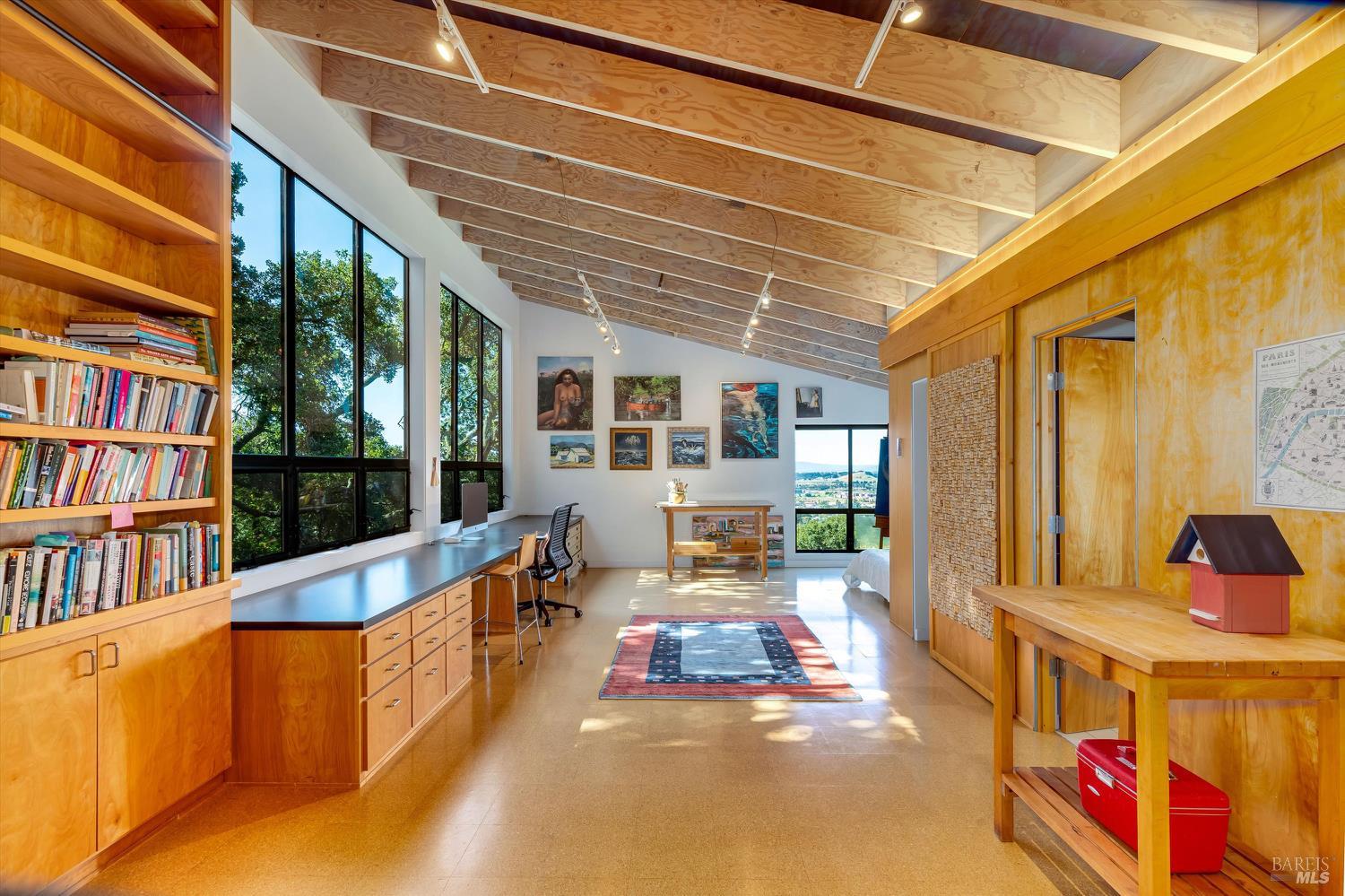 Furnished home office with built-in bookshelves, tall windows, and a vaulted exposed-wood ceiling.