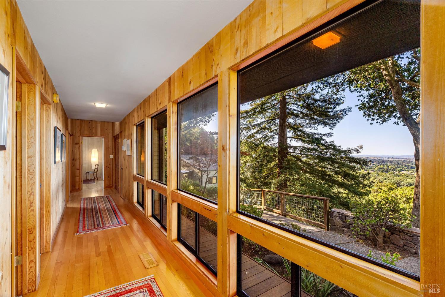 Wood-paneled hallway with large windows overlooking trees and a distant valley.