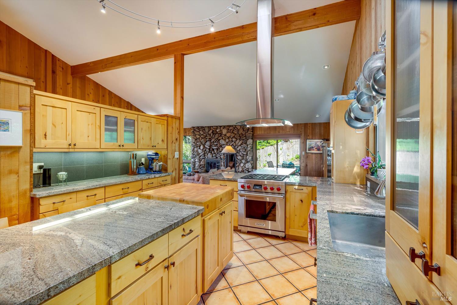 Kitchen with light wood cabinets, granite counters, a central island, and a stone fireplace beyond.