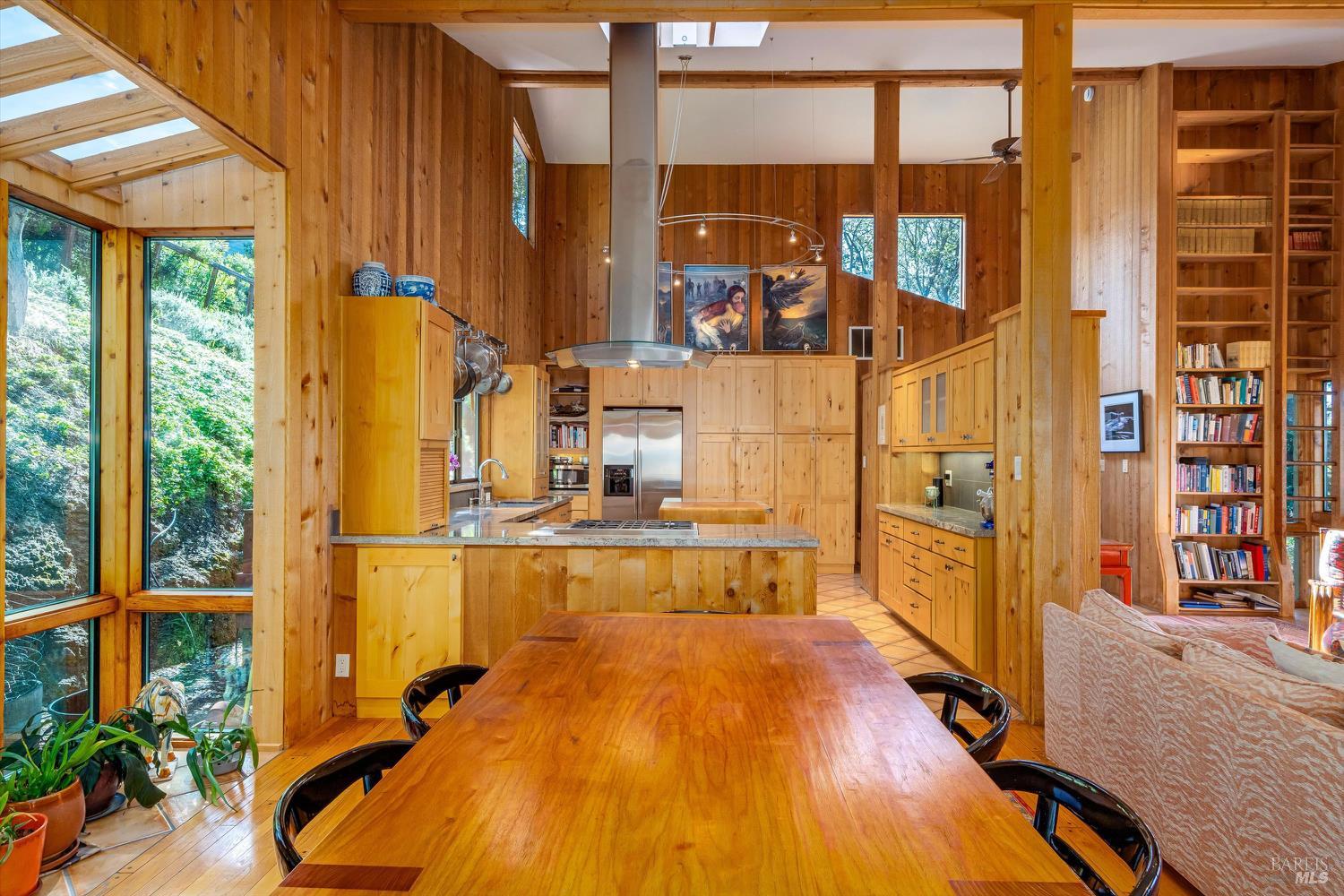 Wood-paneled kitchen and dining area with skylights, large windows, and a long wooden table.