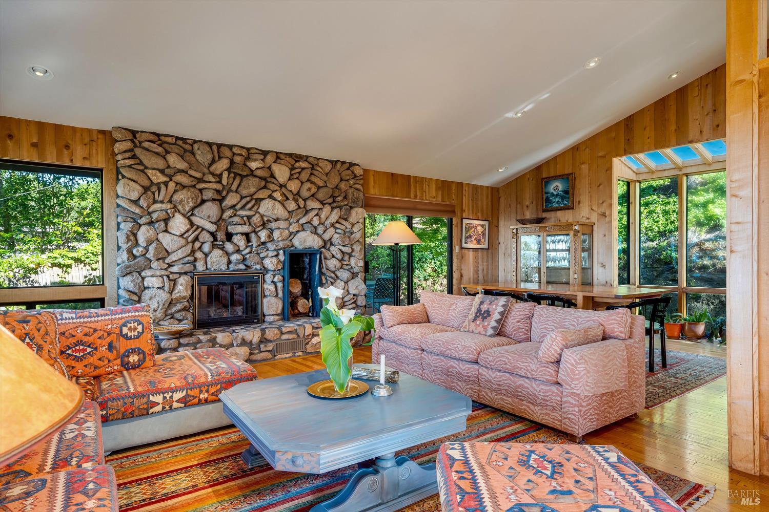 Living room with a stone fireplace, wood-paneled walls, and colorful patterned seating.