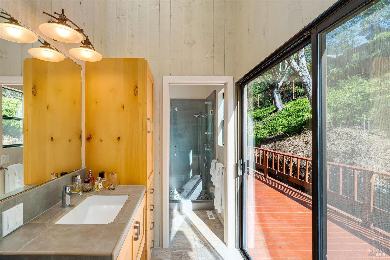 Bathroom with knotty-wood cabinets, a glass shower, and sliding doors to a hillside deck.
