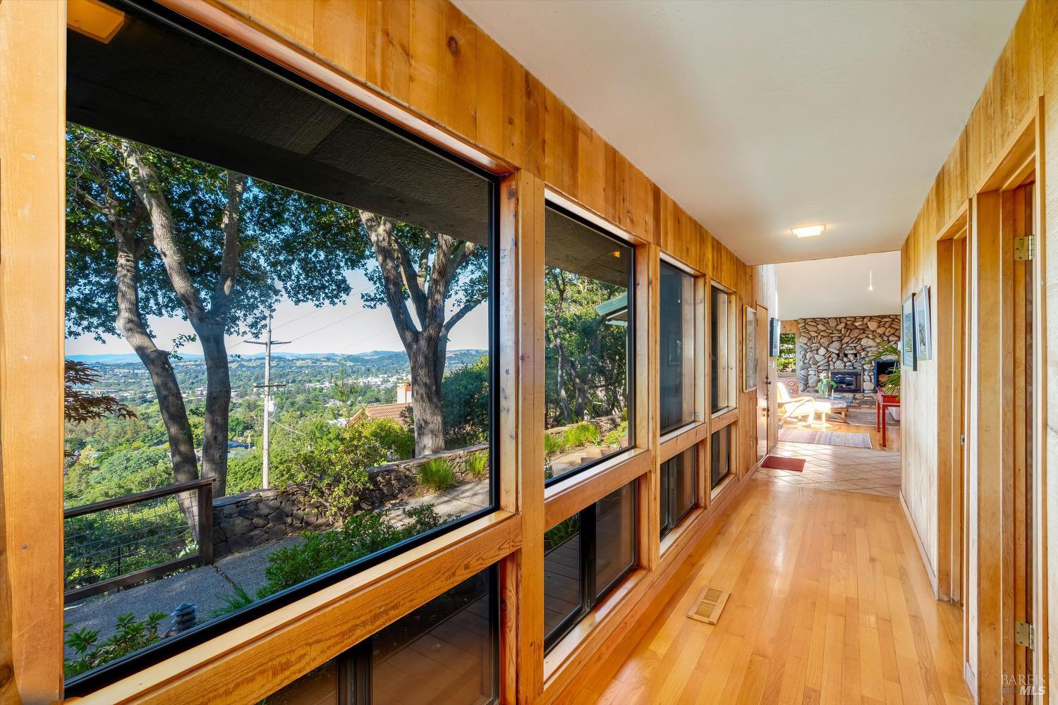 Wood-paneled hallway with expansive windows overlooking leafy grounds and distant hills.