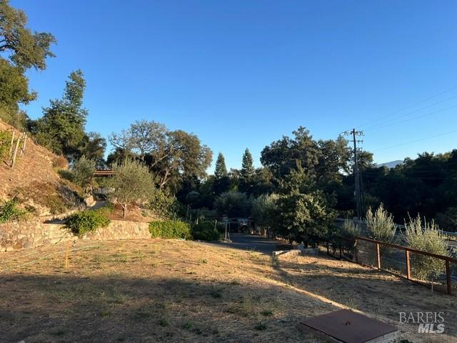 Open lot with a stone retaining wall, planted hillside, mature trees, and metal fencing.