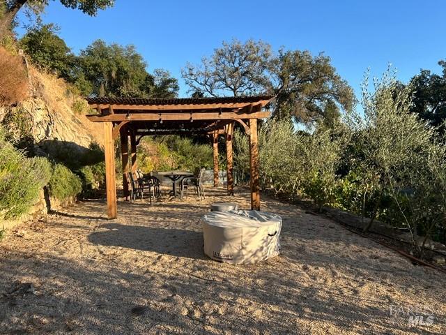 Gravel patio with a wooden pergola, outdoor dining set, and circular concrete fire pit.
