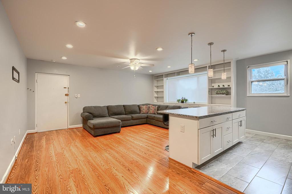 Open-plan living room and kitchen with a gray sectional, white island, hardwood floors, and built-in shelving.