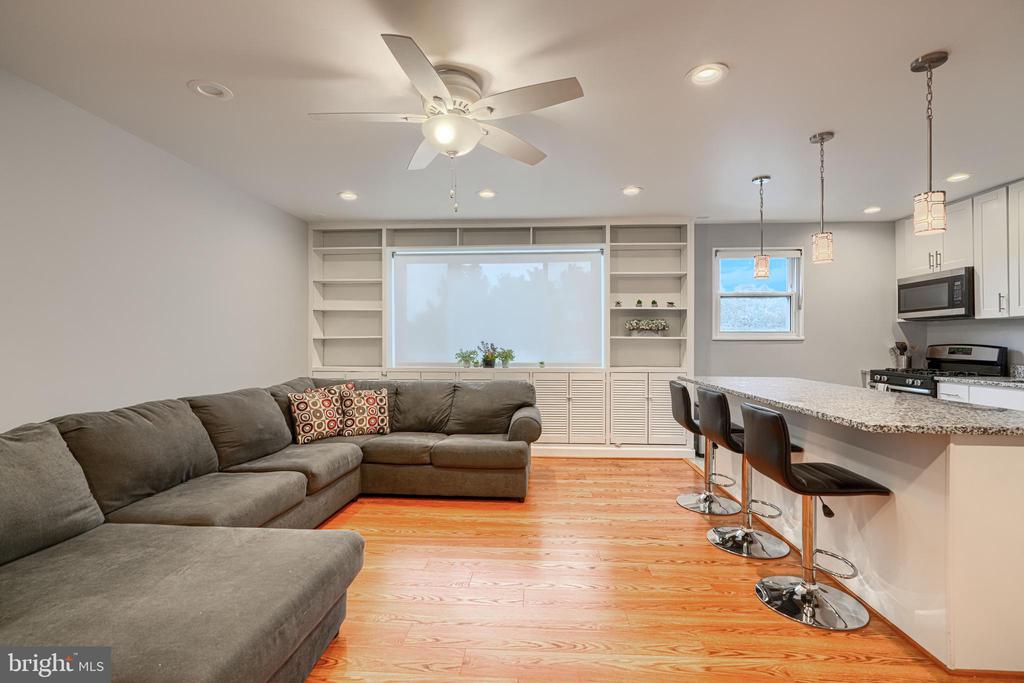 Open-plan living room with a gray sectional, built-in shelves, wood floors, and a granite breakfast bar.