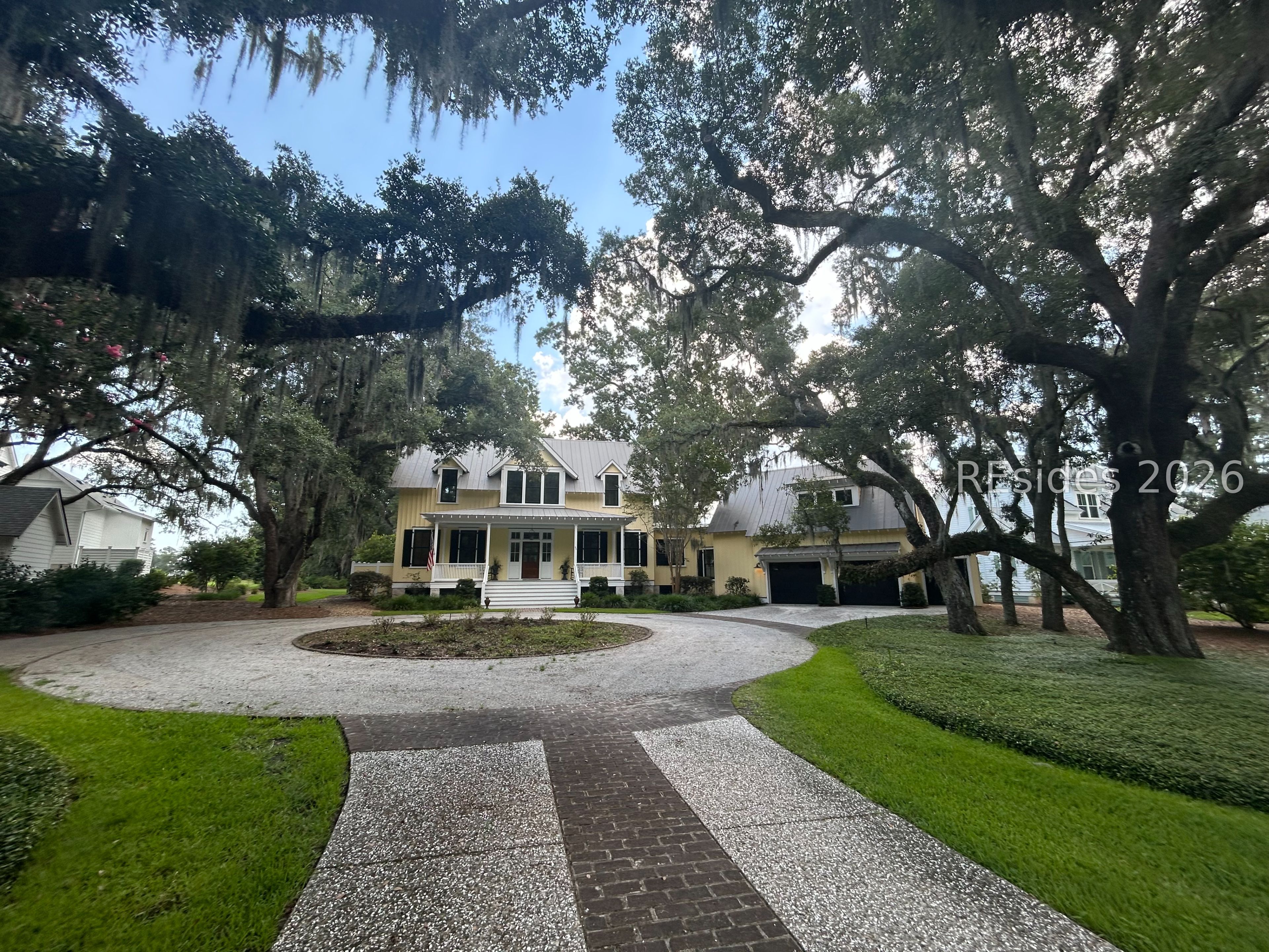 Yellow two-story home with a metal roof, circular driveway, and moss-draped oak trees.