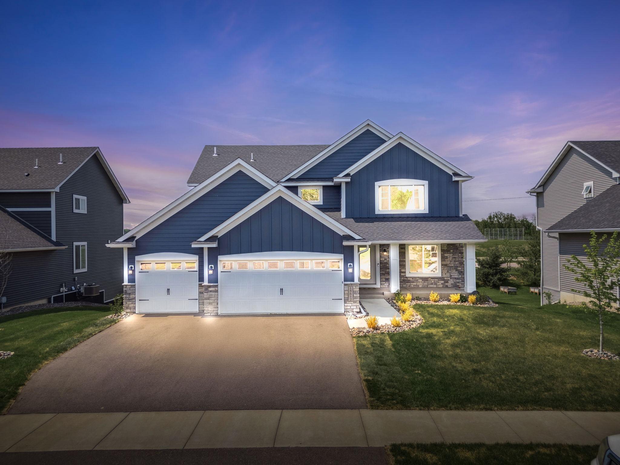 Blue two-story home with two garages and stone accents, photographed at dusk.