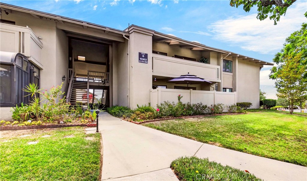 Two-story condominium exterior with an open staircase, landscaped walkway, and fenced patio.