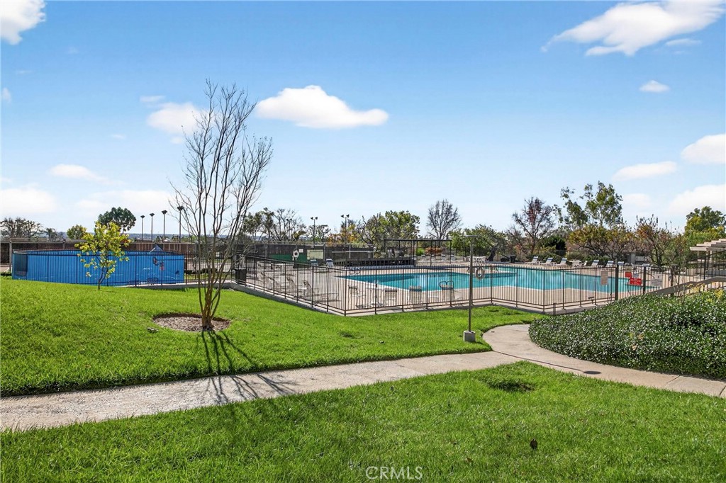 Community swimming pool behind a fence, bordered by a green lawn and curved walkway.
