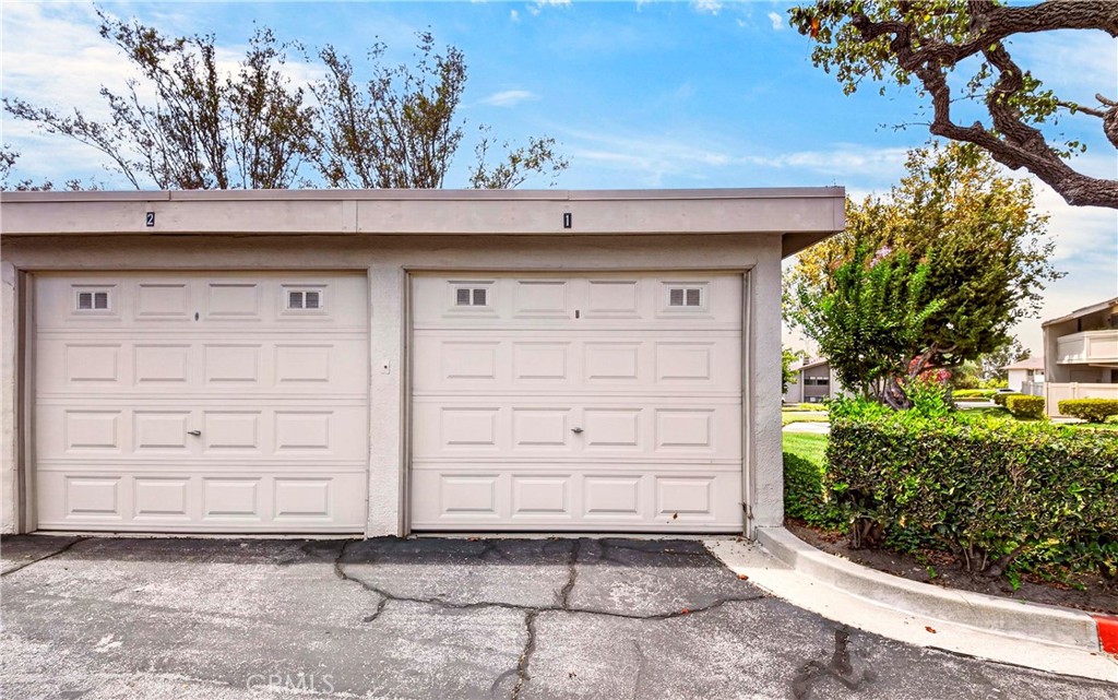 Two white garage doors numbered 2 and 1, with cracked asphalt and landscaped grounds nearby.