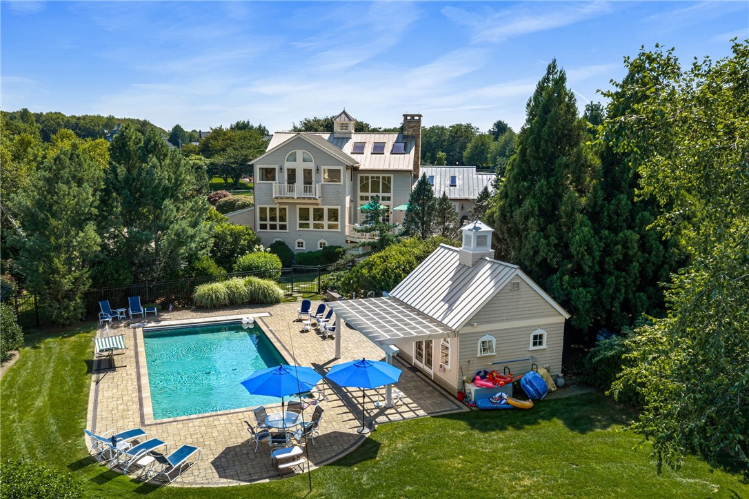 Aerial view of a gray home with a backyard pool, blue umbrellas, and a detached pool house.