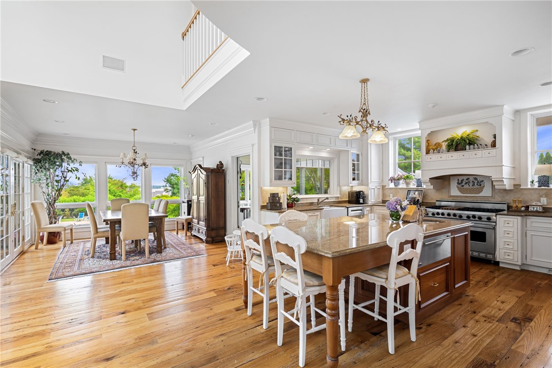 Open kitchen and dining area with a large granite island, hardwood floors, and windows overlooking greenery and water.
