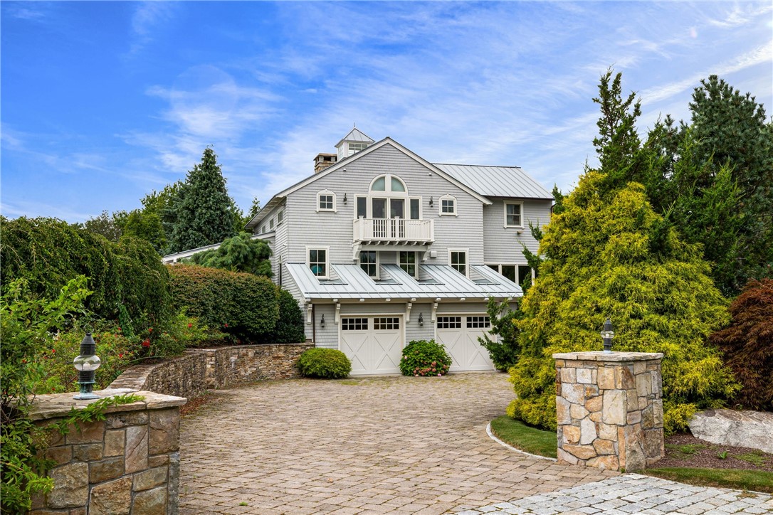 Gray home with metal roof and double garages, approached by a stone-paver driveway between stone pillars.
