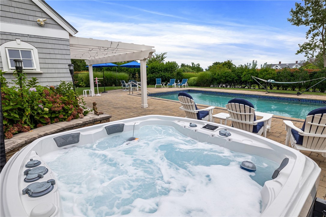 Backyard hot tub and swimming pool beside a gray-shingled home and white pergola.