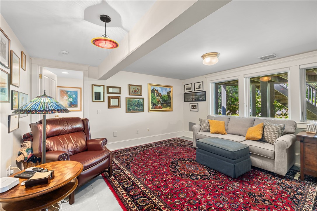 Living room with a gray sofa, leather armchair, patterned red rug, and large windows.