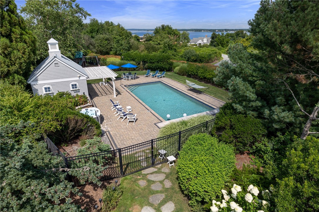Aerial view of a backyard pool and stone patio, with shoreline visible beyond the trees.