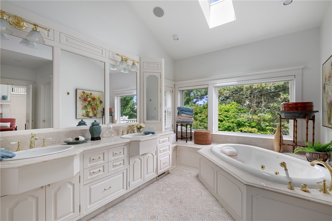 Bright bathroom with a double vanity, soaking tub, skylight, and windows overlooking greenery.