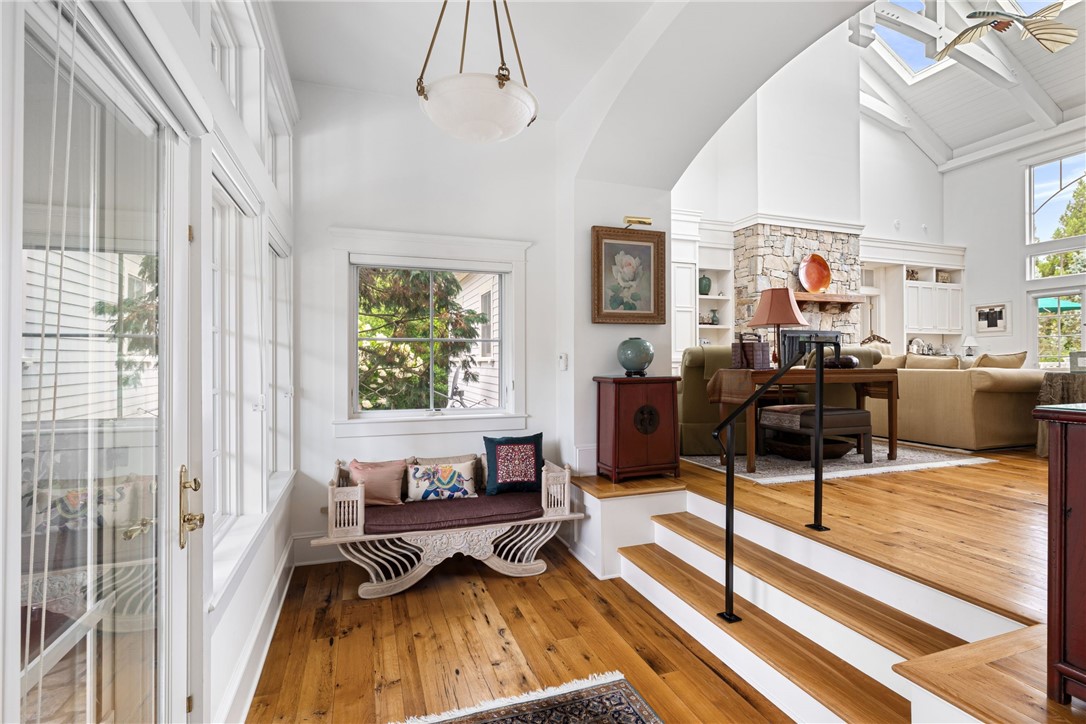Living room with vaulted ceiling, stone fireplace, hardwood floors, and a window-side seating nook.