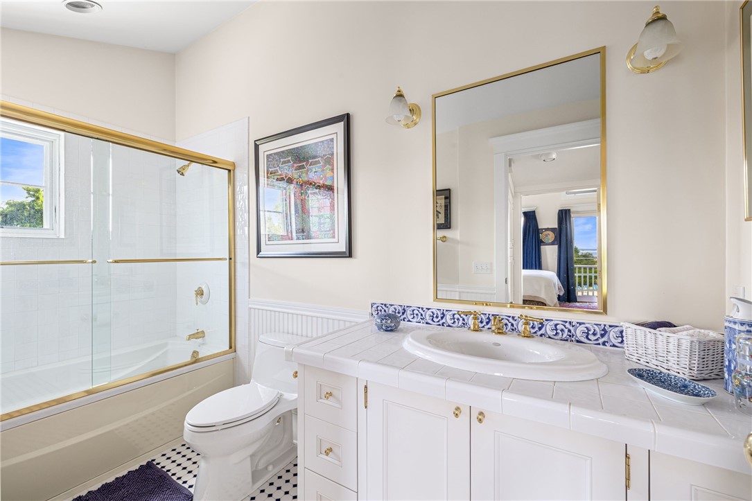 Bright bathroom with gold-trimmed tub doors, blue-and-white tile accents, and a white vanity.