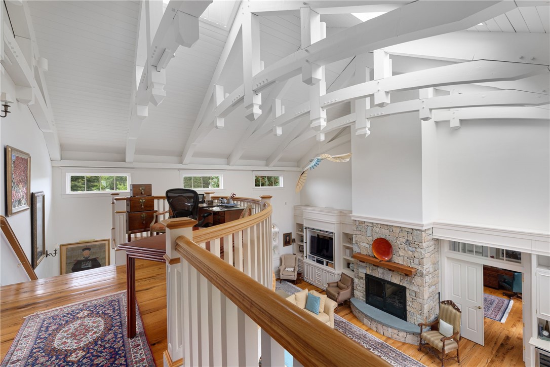 Upper-level gallery overlooking a living room with exposed ceiling beams and a stone fireplace.
