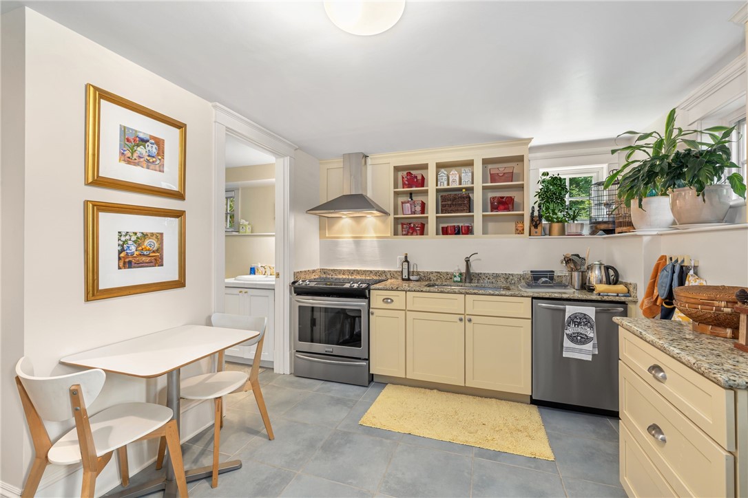 Kitchen with cream cabinets, granite counters, stainless appliances, open shelves, and a small breakfast table.